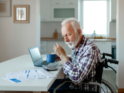 Older white man in wheelchair looking at medical bills 