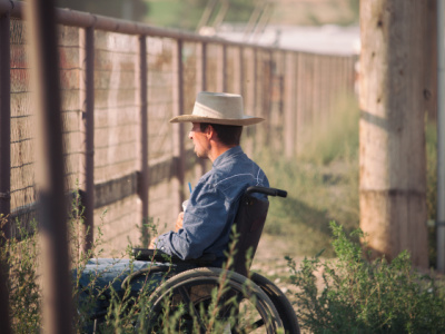 Man in wheelchair in rural area looking at fence
