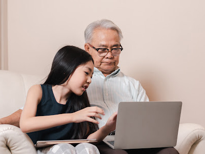 Young girl helping grandfather use laptop